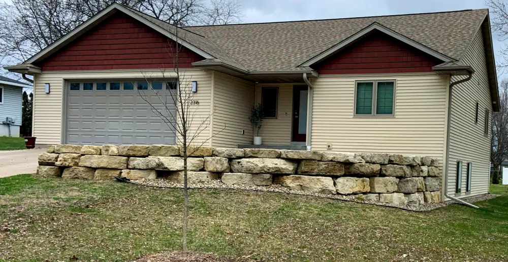 Single story house with a stacked stone retaining wall along the front lawn