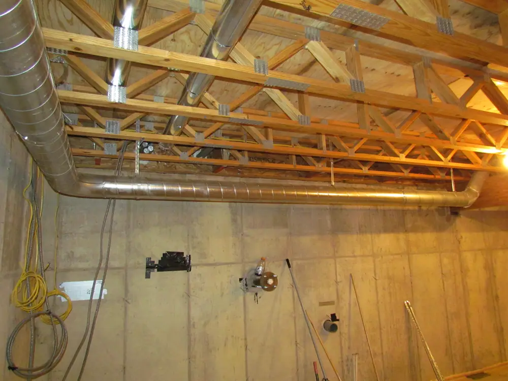 Open ceiling showing wooden trusses, wiring and metal ductwork before drywall