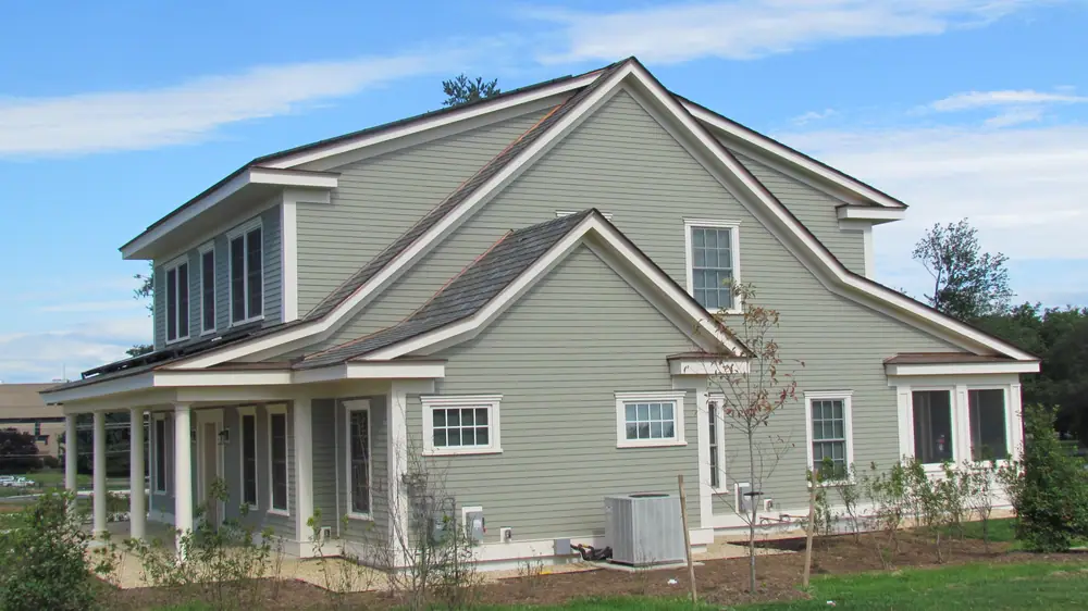 Light green two-story house with white trim and a shingled roof on a sunny day